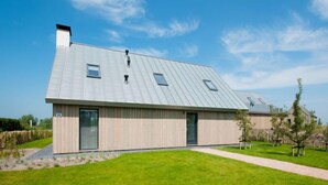 Une maison moderne avec un toit en métal à pente, une grande porte d’entrée et une pelouse bien entretenue.