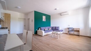 Una sala moderna con una pared de acento color turquesa, un sofá blanco con cojines de colores, una mesita blanca pequeña y un escritorio de madera con una silla.