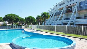 Piscina com hidromassagem, cercada por um muro branco, e um edifício moderno com varandas ao fundo.