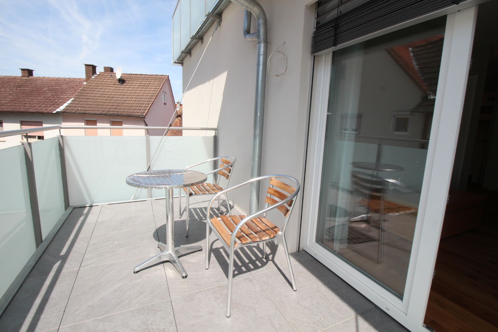 A balcony with a glass door, a metal table, and two chairs.