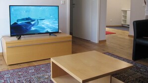 Ett vardagsrum med en platt-TV placerad på ett träskåp, ett litet träbord och en mönstrad matta.