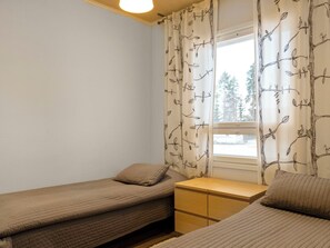A small, tidy room with two single beds, a bedside table, and a window with curtains.
