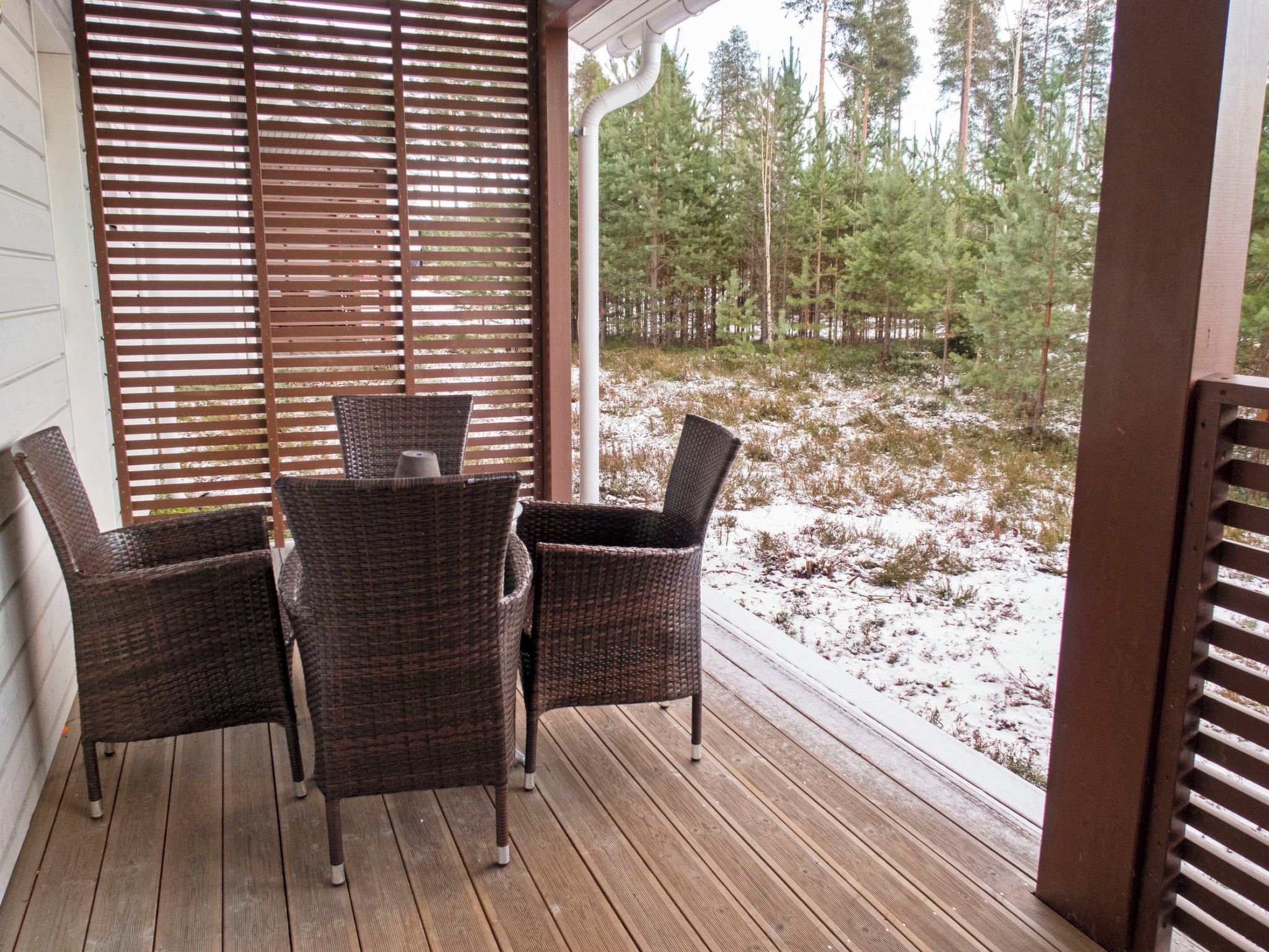 Un espace extérieur abrité, doté d’une terrasse en bois, de chaises en osier et offrant une vue sur un paysage enneigé parsemé d’arbres.