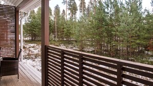 Una terraza de madera con barandilla que da a un área boscosa cubierta de nieve.