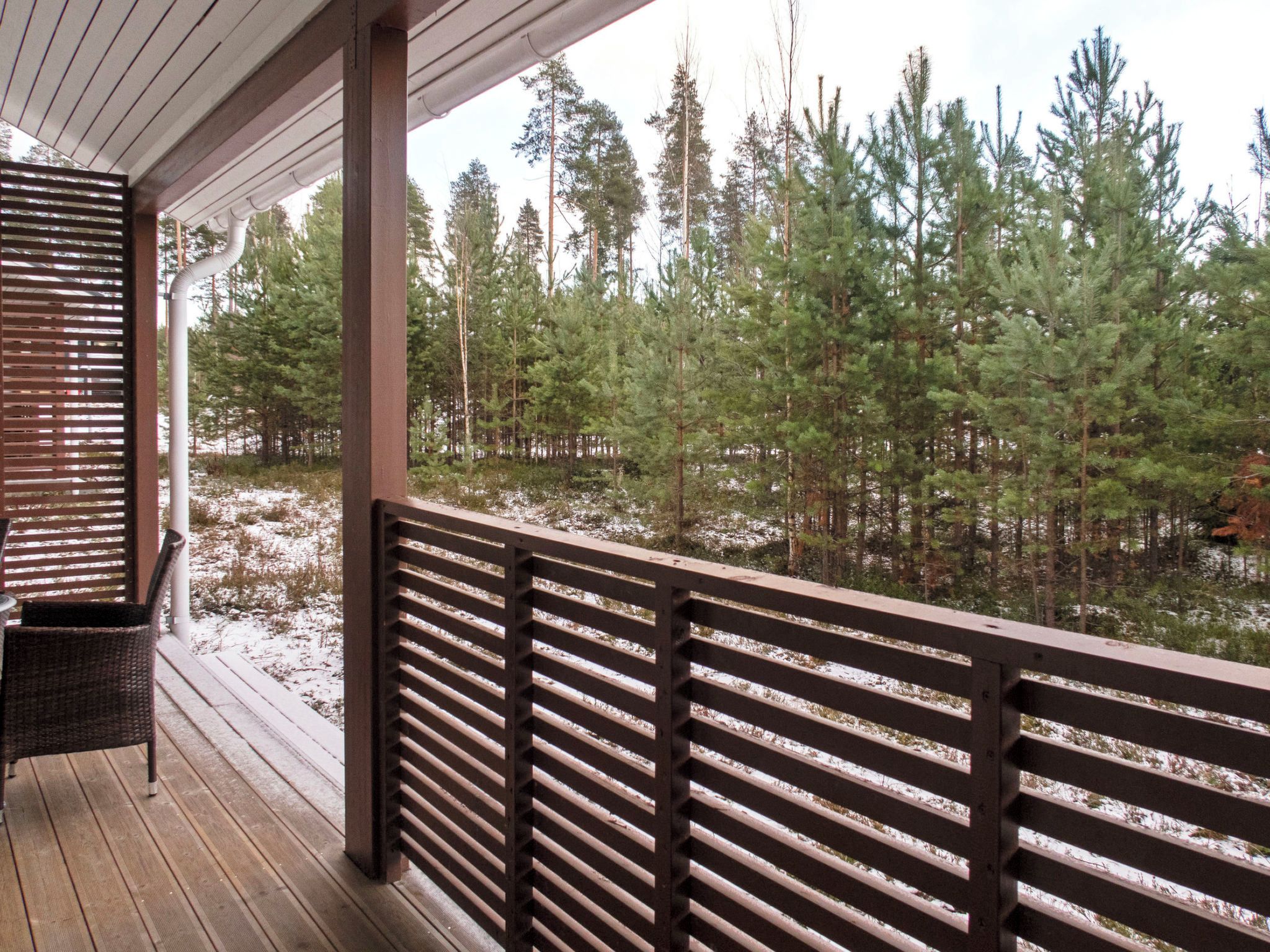 A wooden deck with a railing overlooking a forested area with snow on the ground.