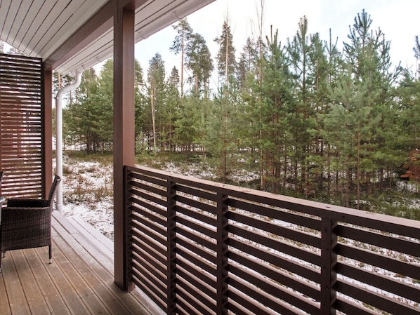 A wooden deck with a railing overlooking a forested area with snow on the ground.
