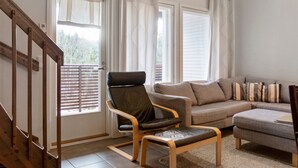 Una sala de estar con una escalera de madera, un sillón de cuero negro, un sofá gris y una mesita.