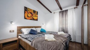 A double bed with a wooden headboard, two bedside tables, a wall-mounted light, and a painting above the bed.