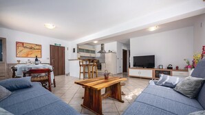 A modern living room with a sofa set, a wooden coffee table, a TV, and a kitchen area in the background.
