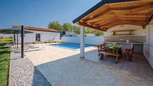 A poolside area with a covered seating area, a barbecue grill, and a small outdoor kitchen.