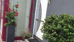 Een modern gebouw met een rode deur, een grote potplant met rode bloemen en een kleine boom.