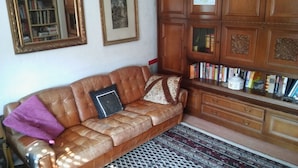 A leather sofa with a patterned throw blanket and pillows, a wooden cabinet with books, and a patterned rug. - 1 room apartment, ground floor, in the 2 Fam.House with garden, GE.-Buer (Gelsenkirchen-Buer, Gelsenkirchen)