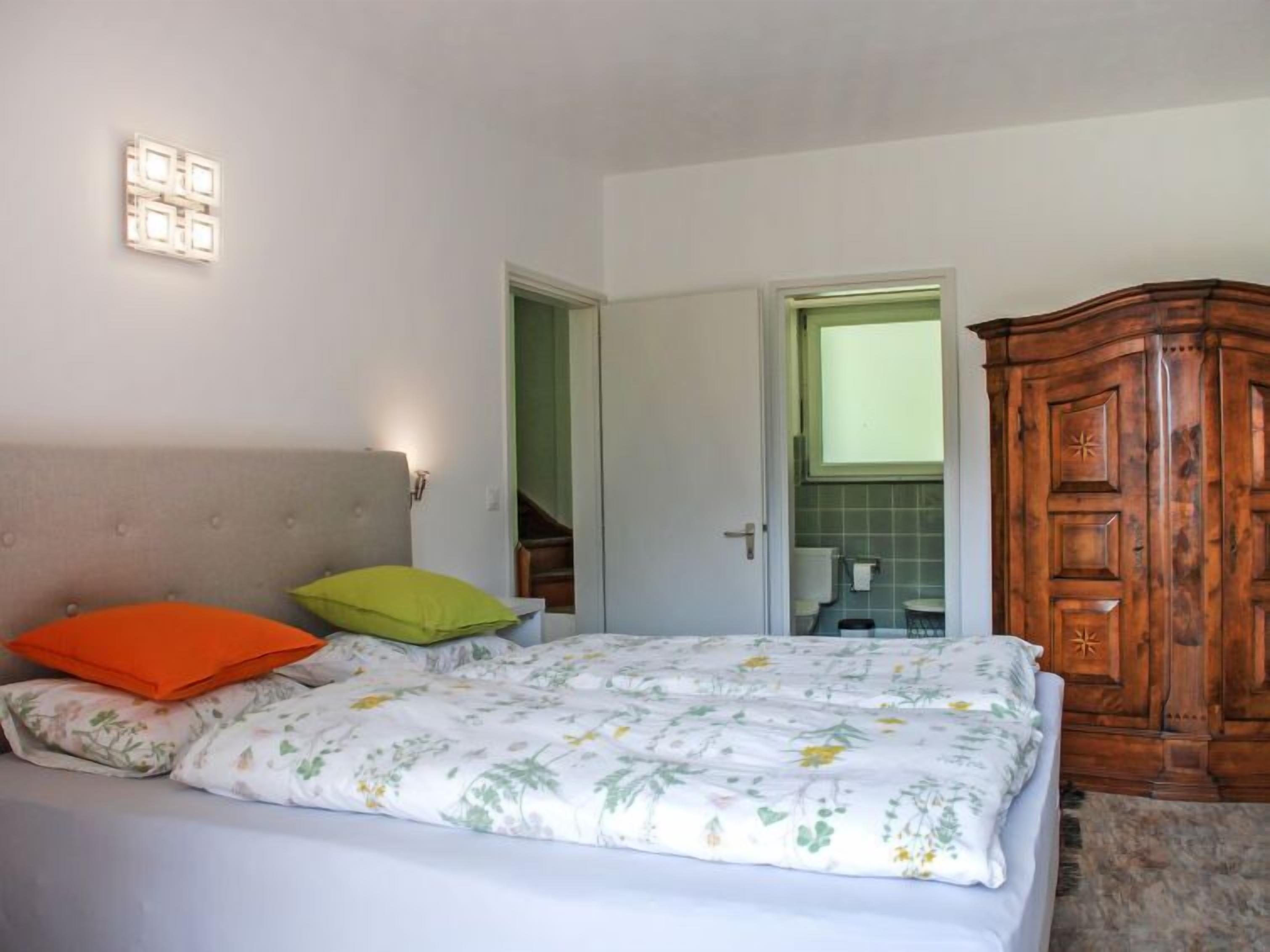 A bedroom with a bed, a wooden wardrobe, and a bathroom visible through an open door.