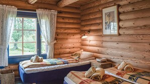Ein gemütliches Cabin-Zimmer mit zwei Betten, einem Fenster mit Vorhängen, einem gerahmten Bild an der Wand und einer Lampe auf dem Nachttisch.