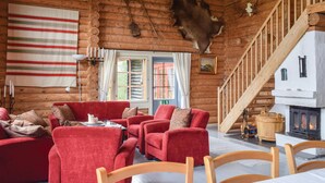 Ein Interieur einer Blockhütte mit rot gepolsterten Sesseln, einem Kamin und einer Holztreppe.