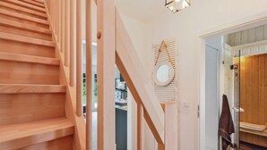 A wooden staircase leading to a room with a mirror, a towel rack, and a view of a kitchen area. - Reetdachhaus 20 auf Usedom (Zirchow/Usedom)