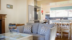 Una sala de estar acogedora con un sofá gris, una mesa de centro de cristal y un comedor con sillas blancas y una mesa de madera.