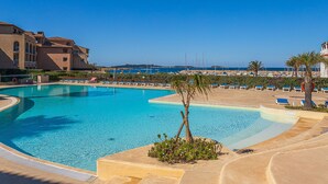 A resort pool area with clear blue water, lounge chairs, and a view of the sea. - Les Rivages de Coudoulière by Interhome (Six Fours La Coudoulière)