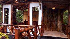 Una estructura de madera con terraza de madera, paredes de bambú y barandilla de madera.