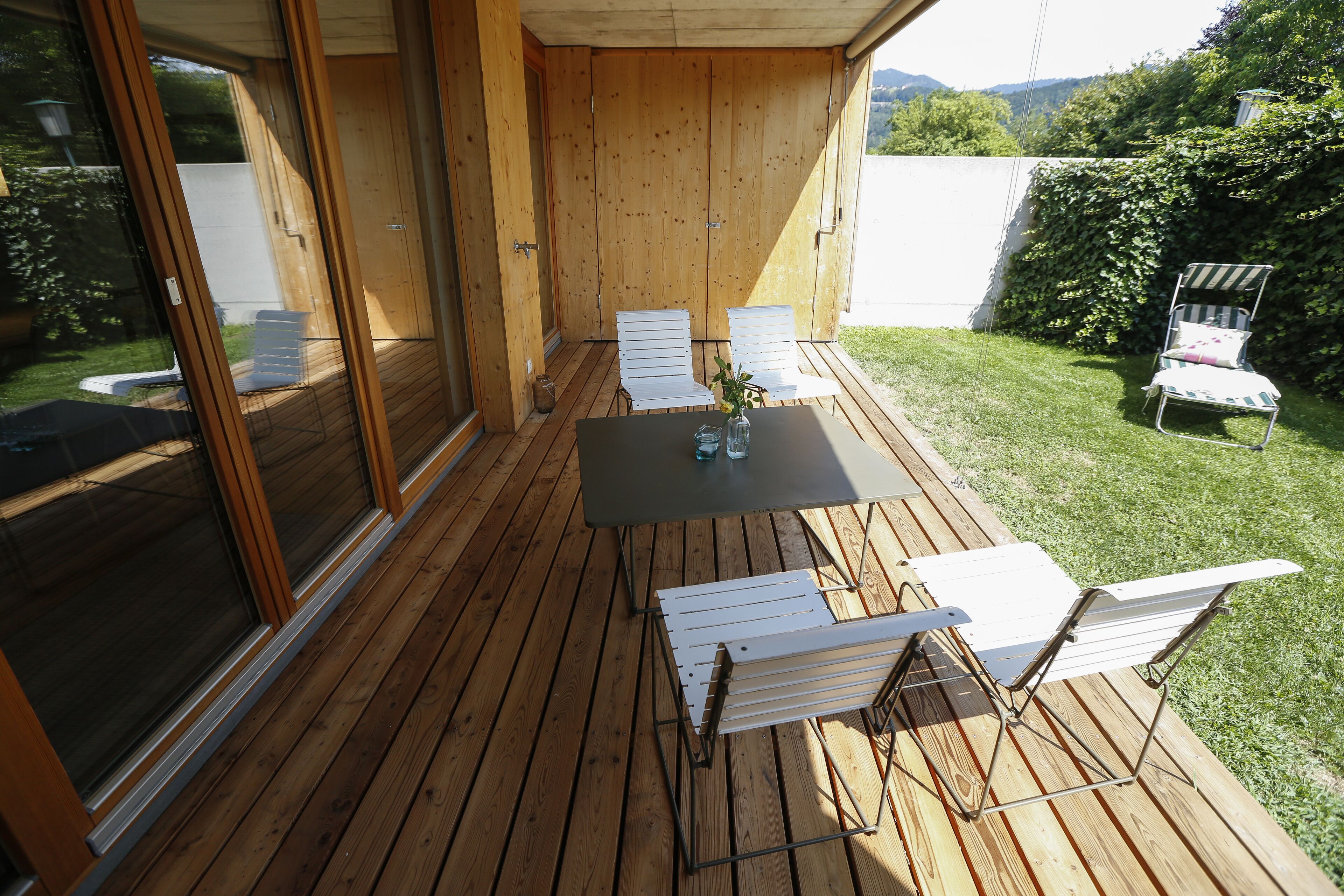 An outdoor deck with a table and chairs, a sliding glass door, and a view of a grassy yard.
