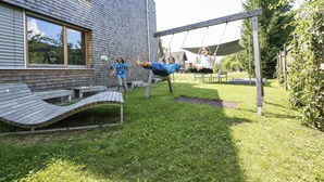 A backyard with a swing set, a wooden deck, and a brick house. - Modern apartment with garden (Klaus)