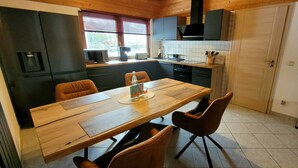 Una cocina con una mesa de madera, dos sillas y un ventanal con persianas.