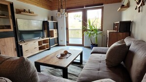 Una sala de estar con un mueble bajo de madera para televisión, un sofá, una mesa de centro y una planta en maceta.
