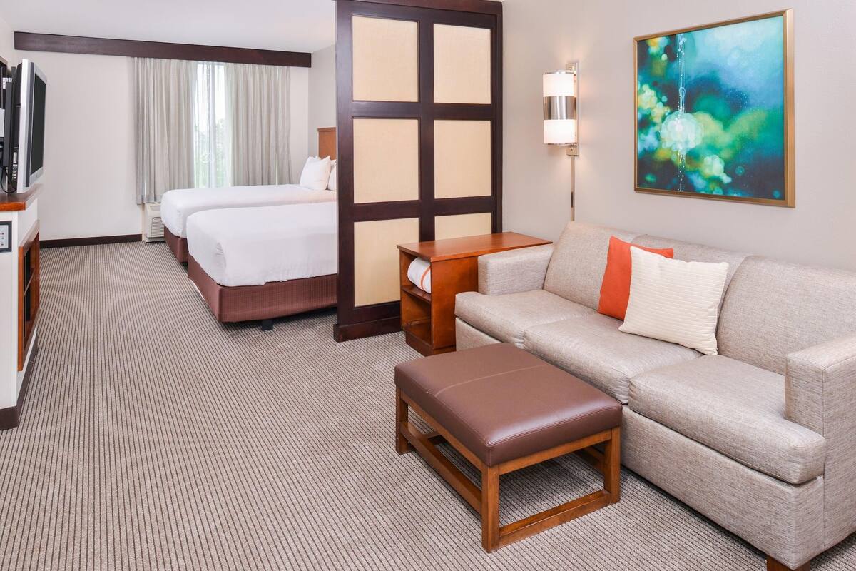 Une chambre d’hôtel avec un lit, un canapé, une petite table, une télévision et un tableau au mur.