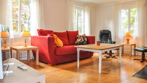 A living room with a red sofa, a wooden coffee table, and two lamps. There are two windows with curtains, and a chair is visible in the background. - Amazing home in årjäng with WiFi (Årjäng)