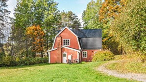 A red barn-style house with a black roof, surrounded by trees and a grassy yard. - Amazing home in årjäng with WiFi (Årjäng)