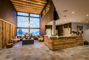 Un vestíbulo moderno con un mostrador de recepción de madera, zona de estar y grandes ventanales con vistas al exterior.