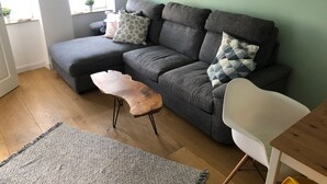 Uma sala de estar com um sofá seccional cinza, uma mesa de centro de madeira, uma cadeira branca e um tapete estampado.