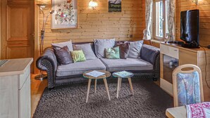 A cozy room with a grey sofa, two small tables, a television, and wooden walls. - Ferienwohnung in Fresach (Fresach)