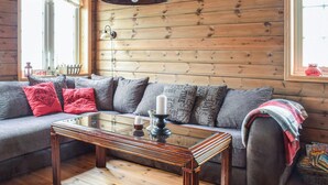 L’intérieur chaleureux d’un chalet en bois, avec un canapé en bois, une table basse en verre et une suspension.
