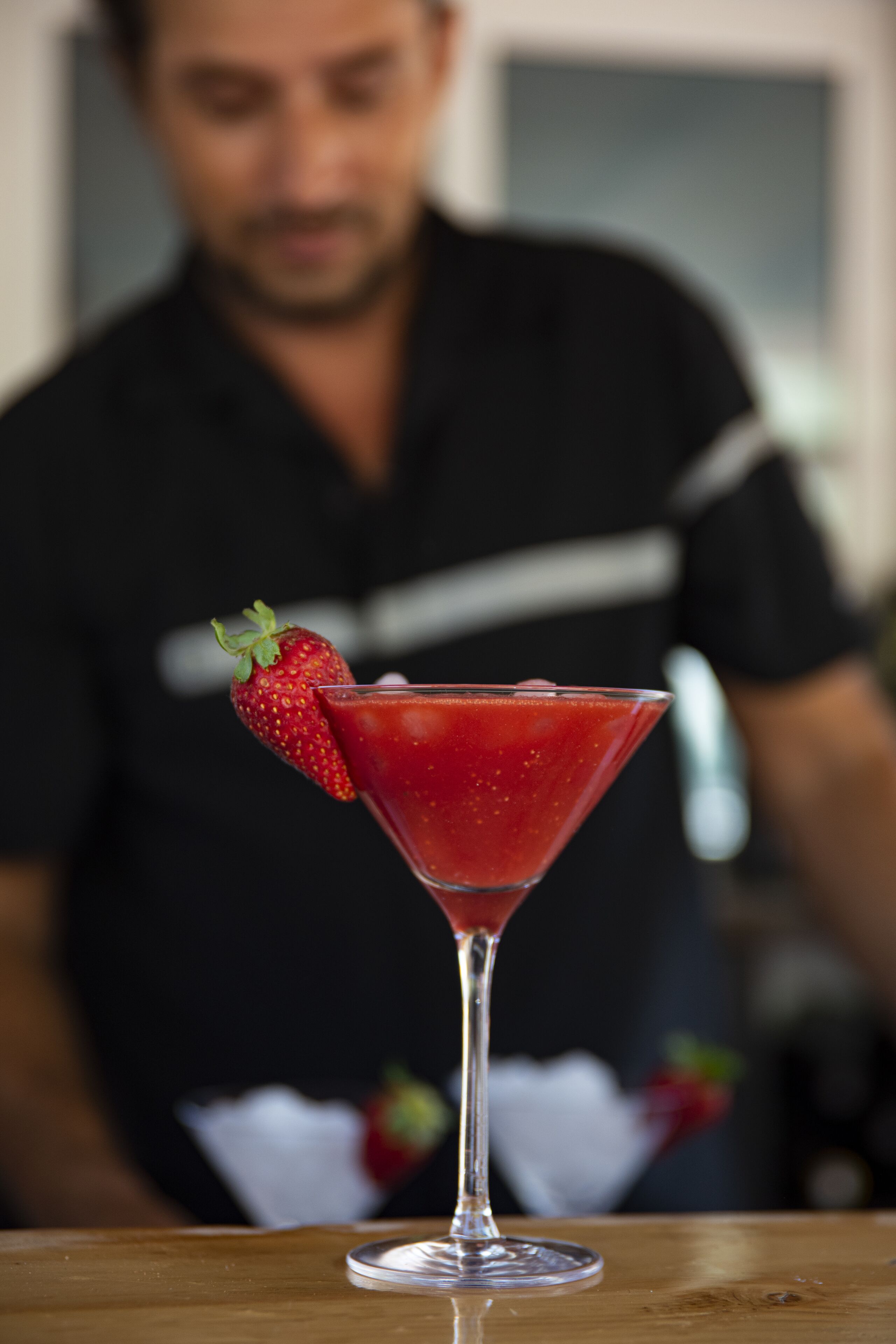 A martini glass with a strawberry garnish on a wooden table.