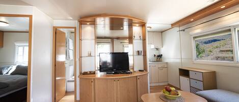 A compact living space with a kitchenette, a television, a dining area with a fruit bowl, and a sofa.