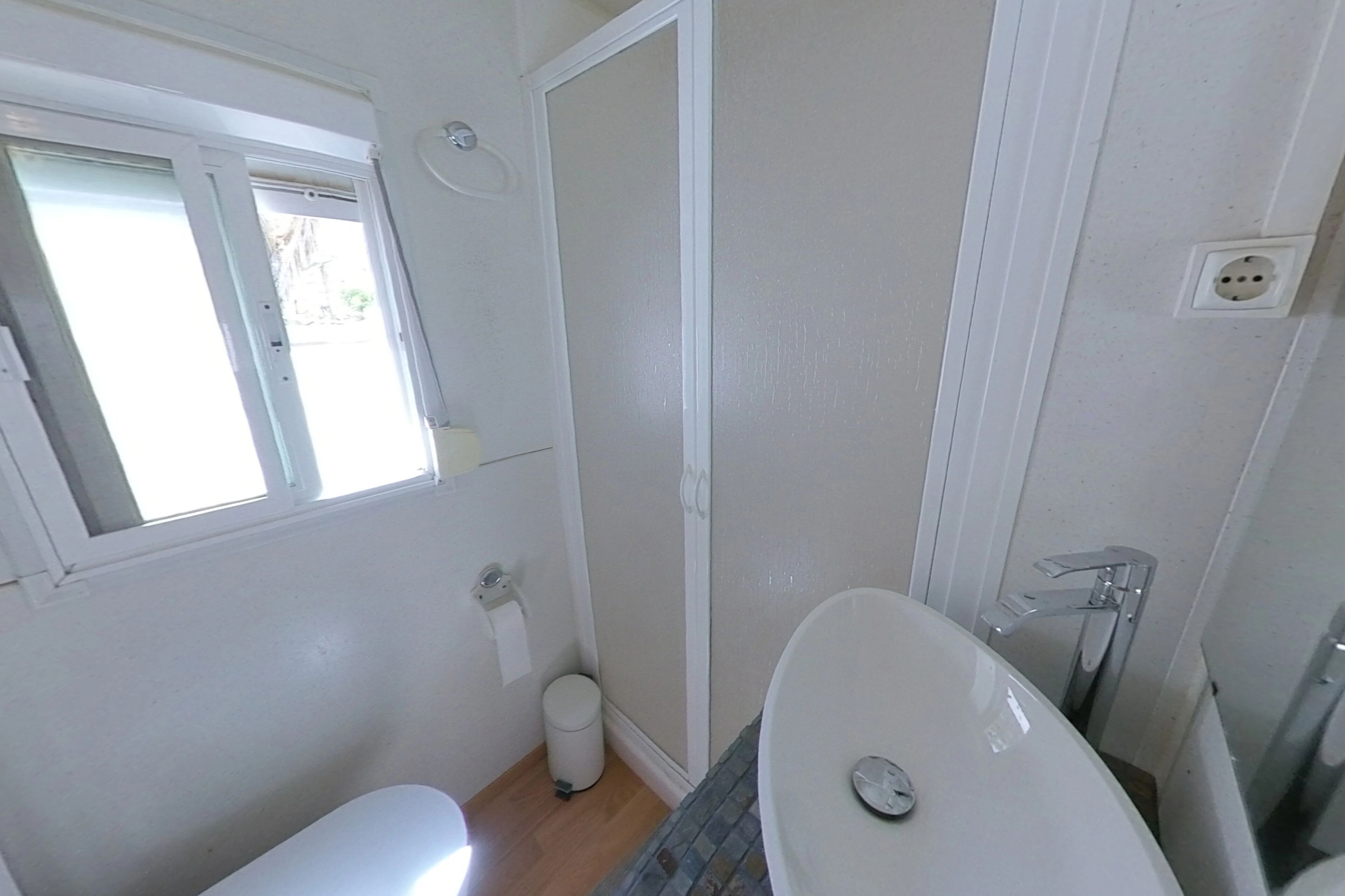 A bathroom with a toilet, sink, shower, and window.