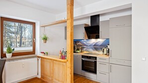 Une cuisine de taille réduite avec une colonne en bois, une fenêtre donnant sur les arbres et un poêle.