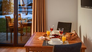 Une table à manger avec des aliments pour le petit-déjeuner, un verre de jus d’orange et un verre de vin rouge.