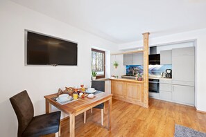 Una cocina moderna con una isla de madera, un comedor con mesa y sillas, y un televisor de pantalla plana grande montado en la pared.