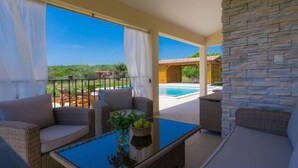 A balcony with wicker furniture, a glass table, and a view of a pool and building. - Vacation home Eugen by Interhome (Barban)