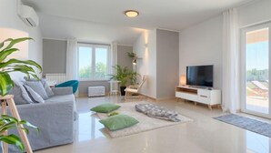A modern living room with a grey sofa, a TV, and a large window. - Vacation home Eugen by Interhome (Barban)