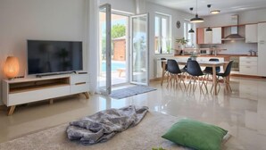 A modern living room with a TV, a dining area, and a kitchen. - Vacation home Eugen by Interhome (Barban)