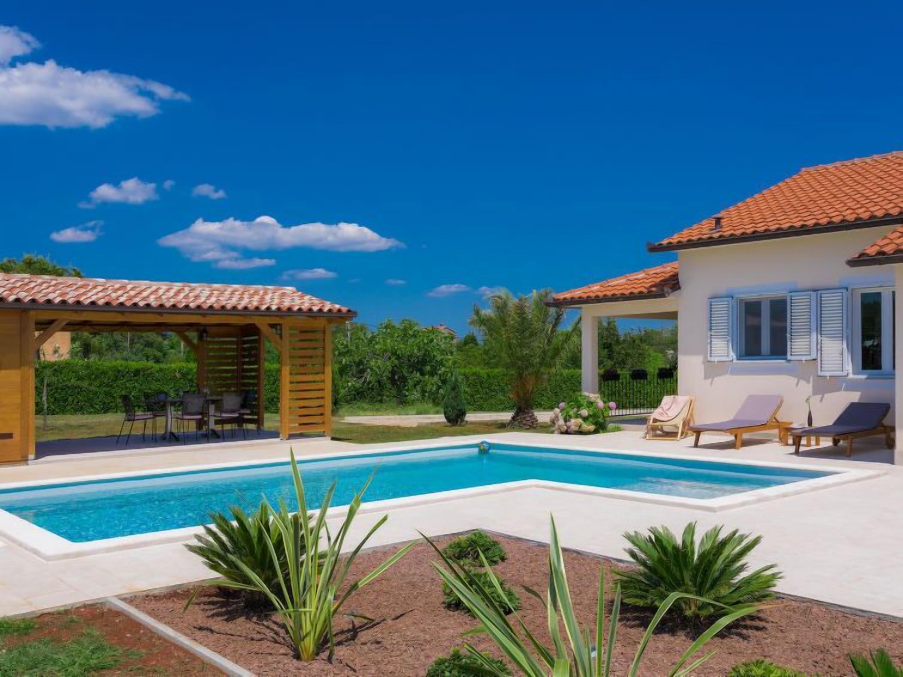 Un espace aménagé au bord de la piscine, comprenant une pergola, des chaises longues et un petit jardin.