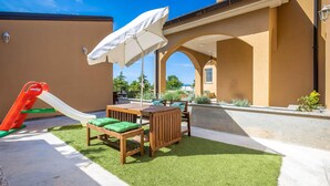 Un patio con mesa y sillas de madera, un tobogán y un paraguas blanco.