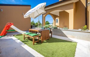 Relax in the shaded patio area with a table and chairs, surrounded by a low wall and artificial grass.