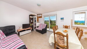 A living room with a sofa, a TV, a bookshelf, a dining table with chairs, and a view through a glass door. - Beautiful apartment in Seget Vranjica (Seget Vranjica)