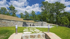 A stone pathway leading to a seating area with a stone wall backdrop, surrounded by grass and trees. - Agr. Castello della Mugazzena by Interhome (Aulla)
