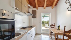 A modern kitchen with a built-in oven, a stove, and a sink. There is a dining area with a table and chairs, and a view of the outdoors through a glass door. - Beautiful home in Zrnovnica-Split with sauna (Zrnovnica-Split)