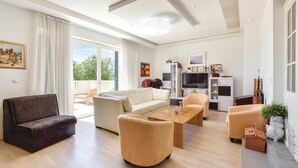 A modern living room with a sofa, armchairs, a coffee table, and a TV. There is a balcony with a view of greenery. - Beautiful home in Zrnovnica-Split with sauna (Zrnovnica-Split)